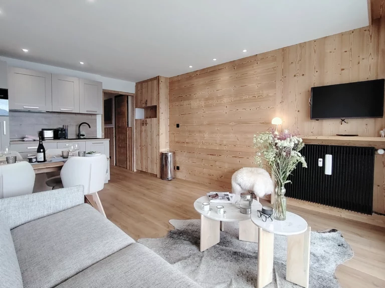 Location appartement à l'alpe d'huez - Pièce de vie avec canapé, table basse, télévision et cuisine à l'arrière plan