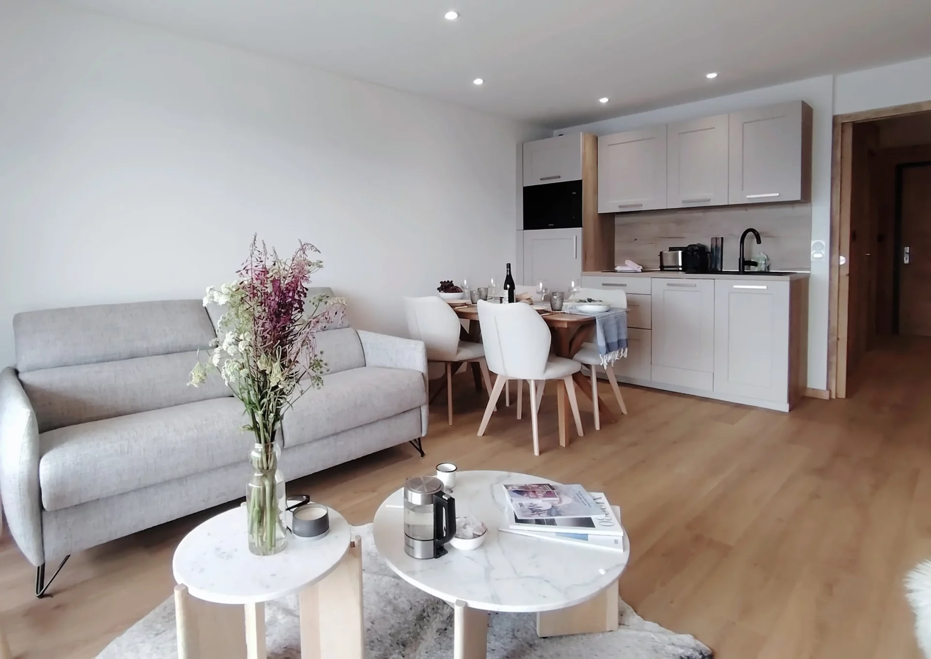 Location appartement à l'alpe d'huez - Pièce de vie avec table dressée au premier plan avec des fruits et des baguettes