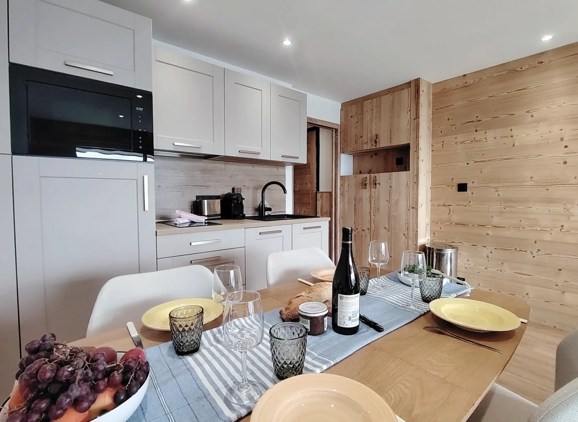 Location appartement à l'alpe d'huez - Pièce de vie avec table dressée au premier plan avec des fruits et des baguettes