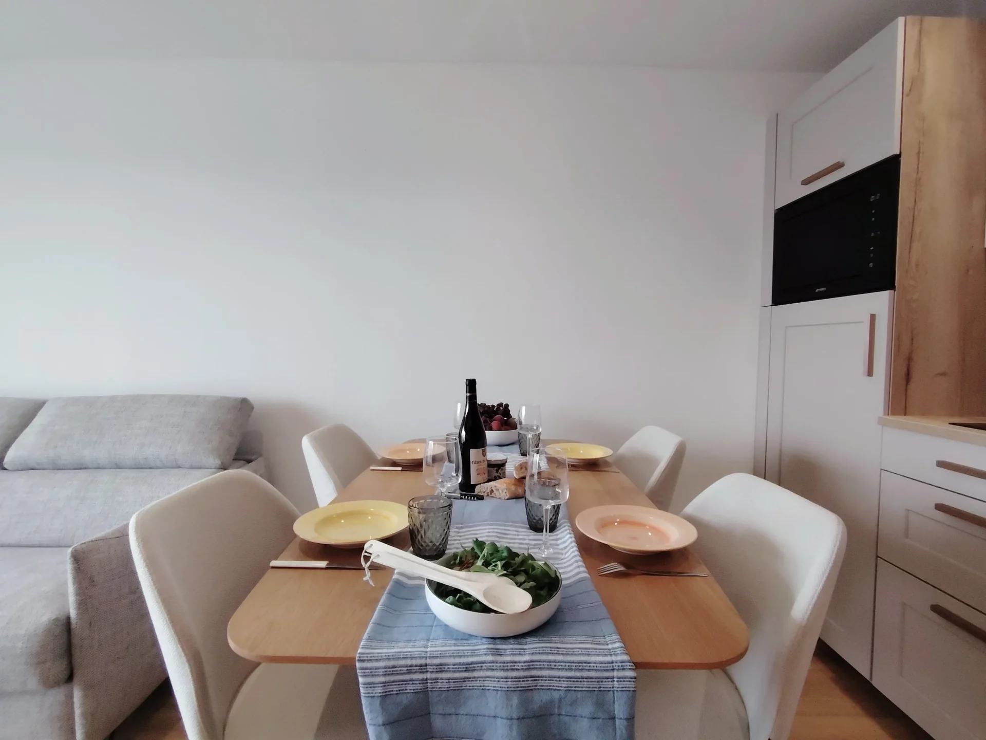 Location appartement à l'alpe d'huez - Pièce de vie avec table dressée au premier plan avec des fruits et des baguettes