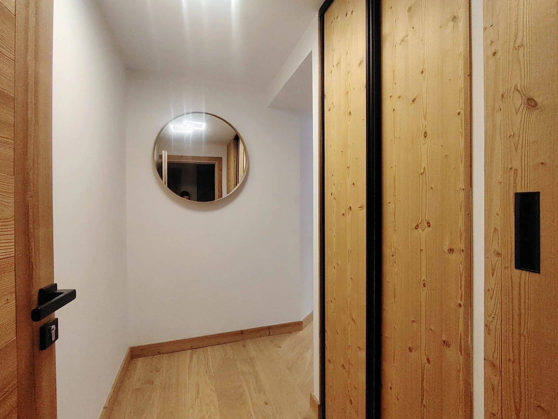 Entrée et dégagement avec miroir rond et rangements en bois – Appartement Cachemire A105