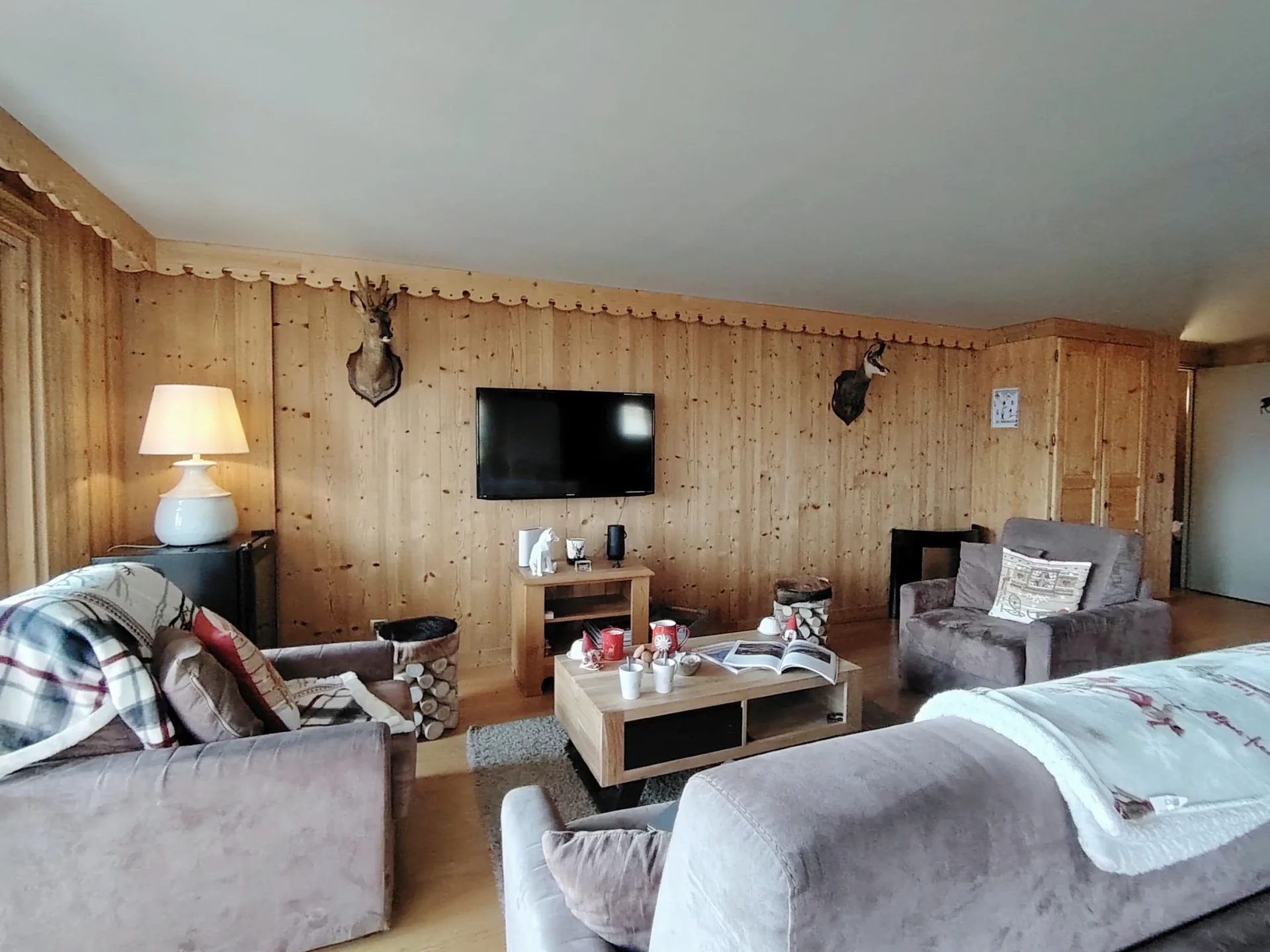 Appartement Les Alpages à l’Alpe d’Huez – salon cosy en bois avec canapés confortables, TV et déco montagnarde – location de vacances au pied des pistes