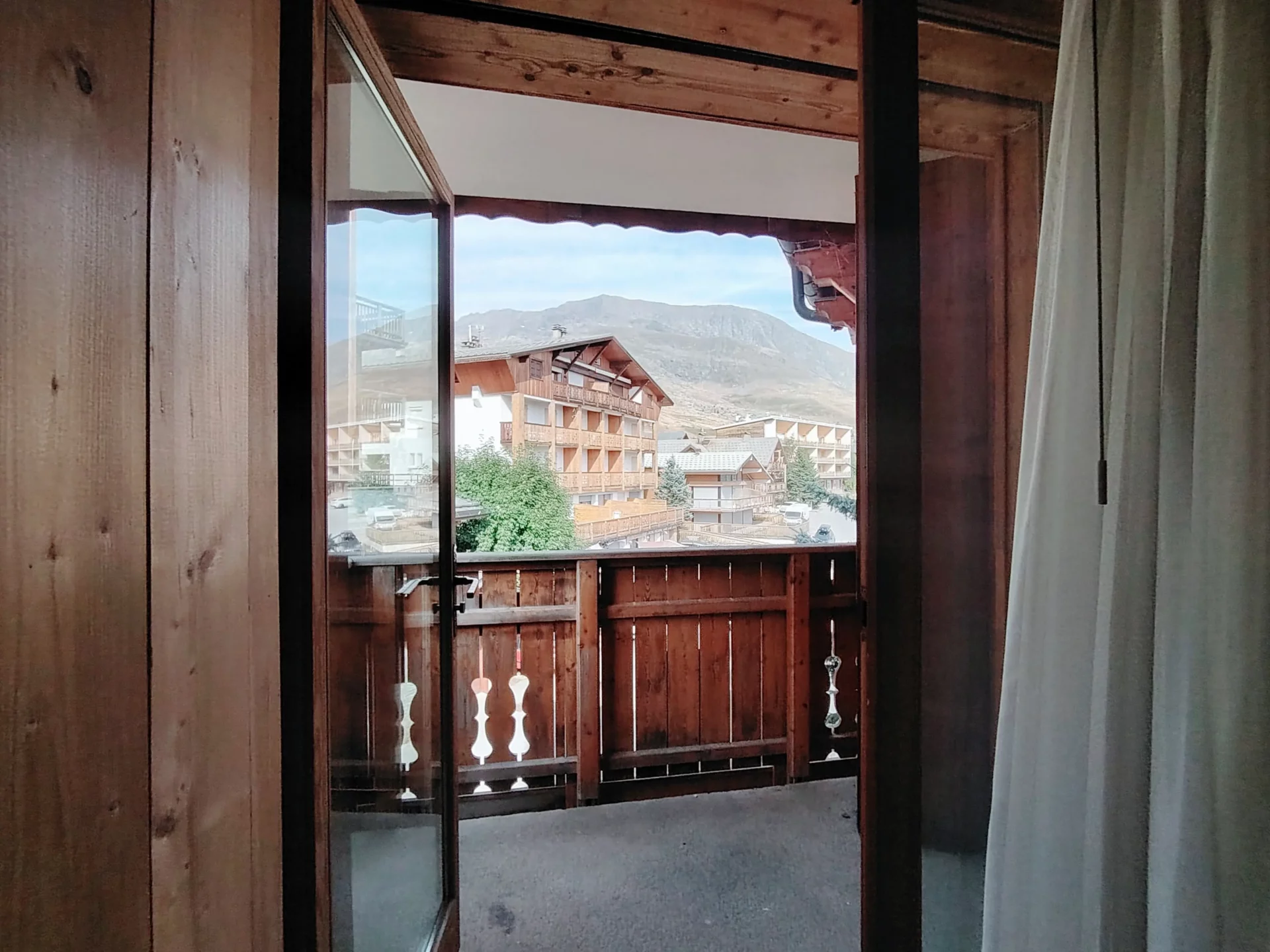 Vue depuis une chambre de l’appartement Les Alpages à l’Alpe d’Huez, balcon privé donnant sur les chalets et montagnes alpines