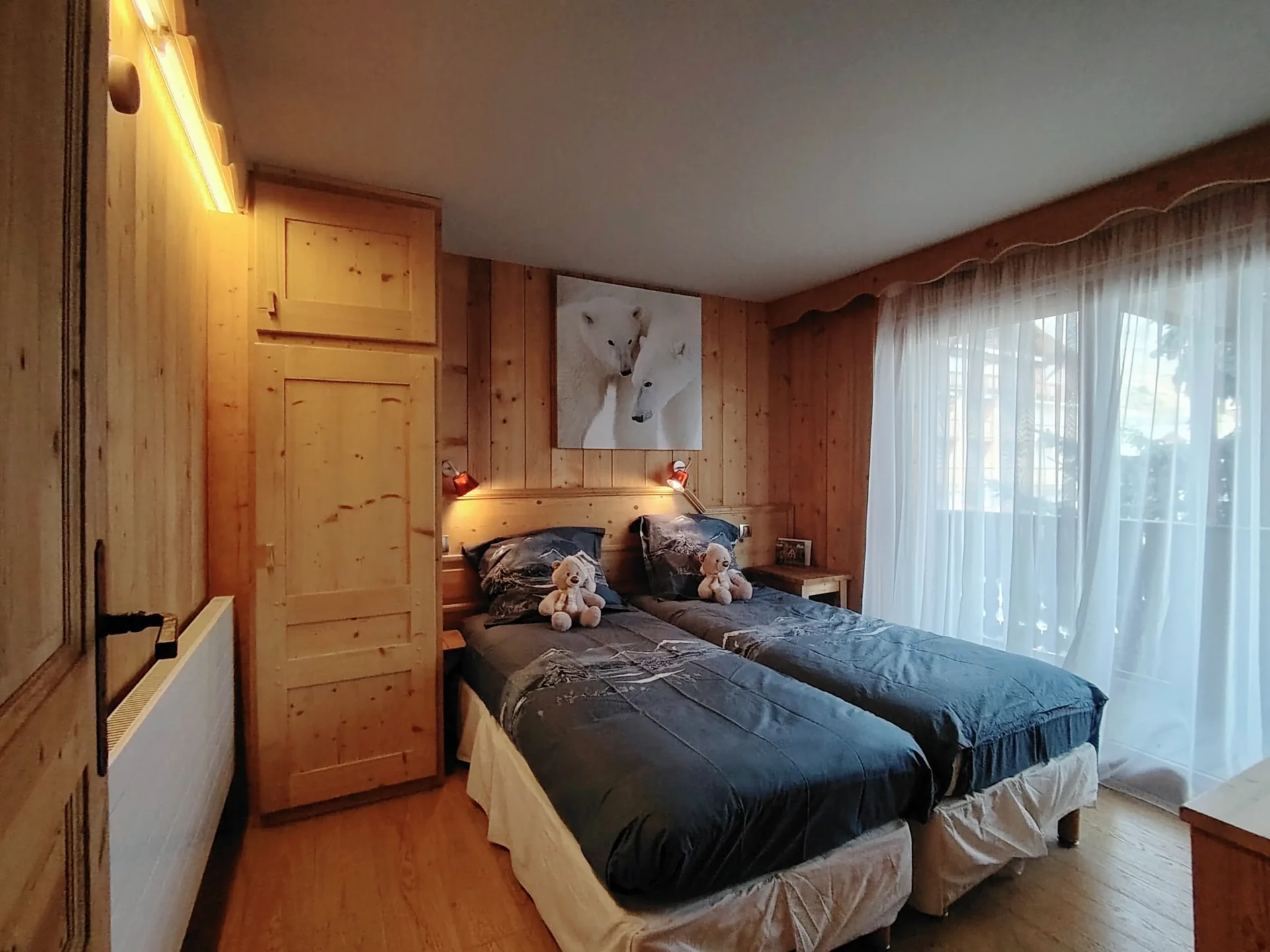 Chambre lumineuse avec deux lits simples de l’appartement Les Alpages à l’Alpe d’Huez, donnant sur un balcon avec vue montagne