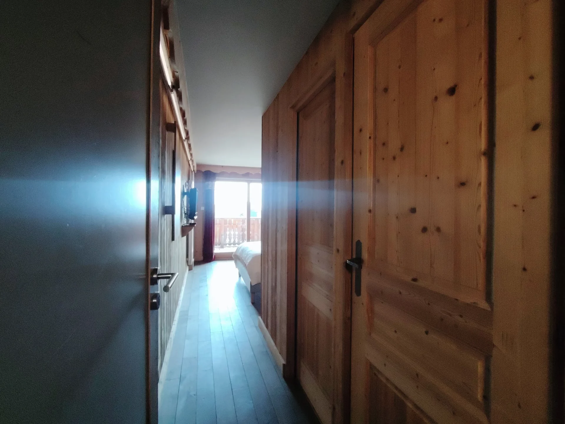 Couloir en bois de l’appartement Les Alpages à l’Alpe d’Huez menant à une chambre avec accès direct au balcon lumineux