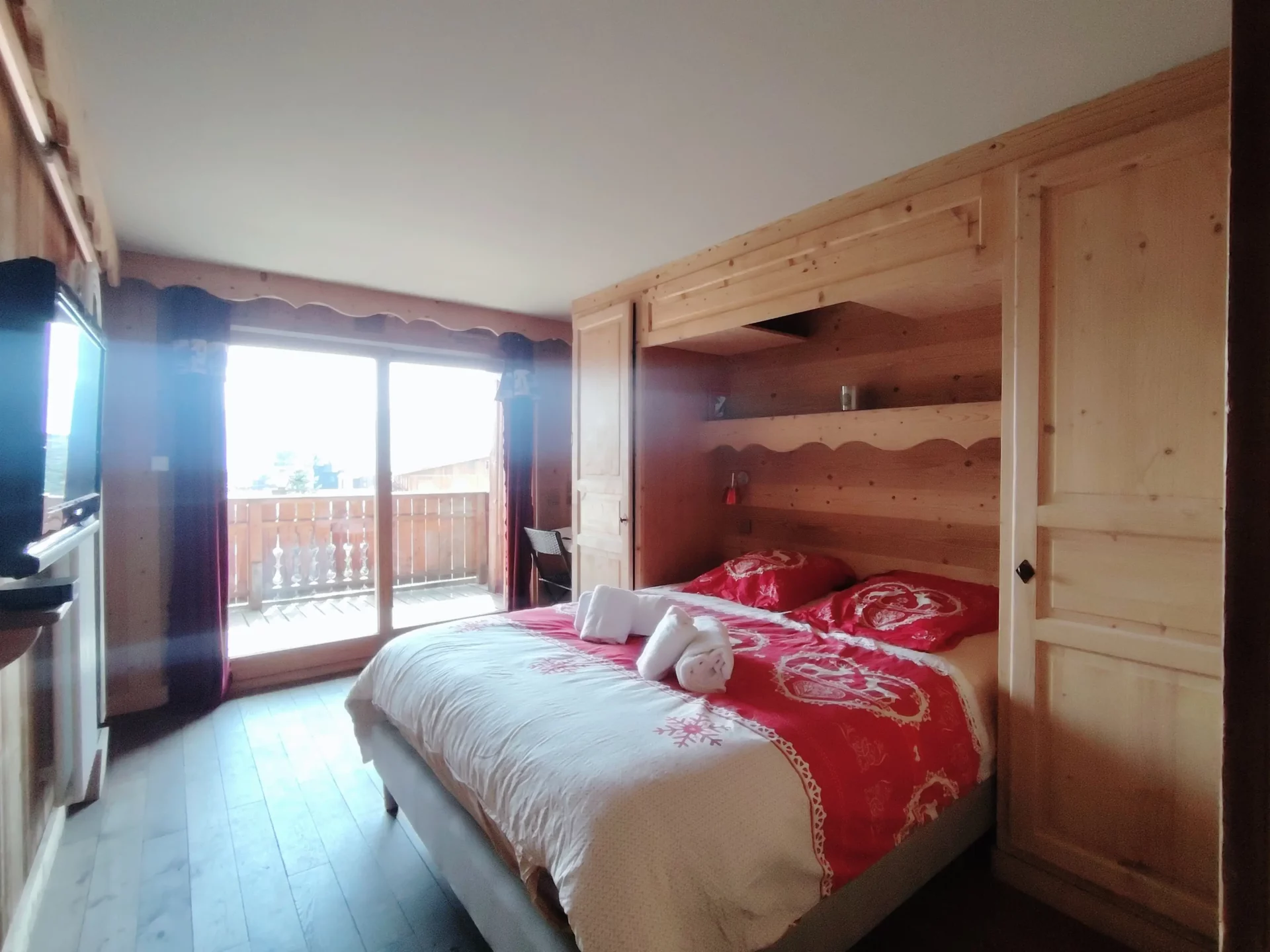 Chambre double de l’appartement Les Alpages à l’Alpe d’Huez, lit confortable avec linge rouge, accès balcon et vue sur la station