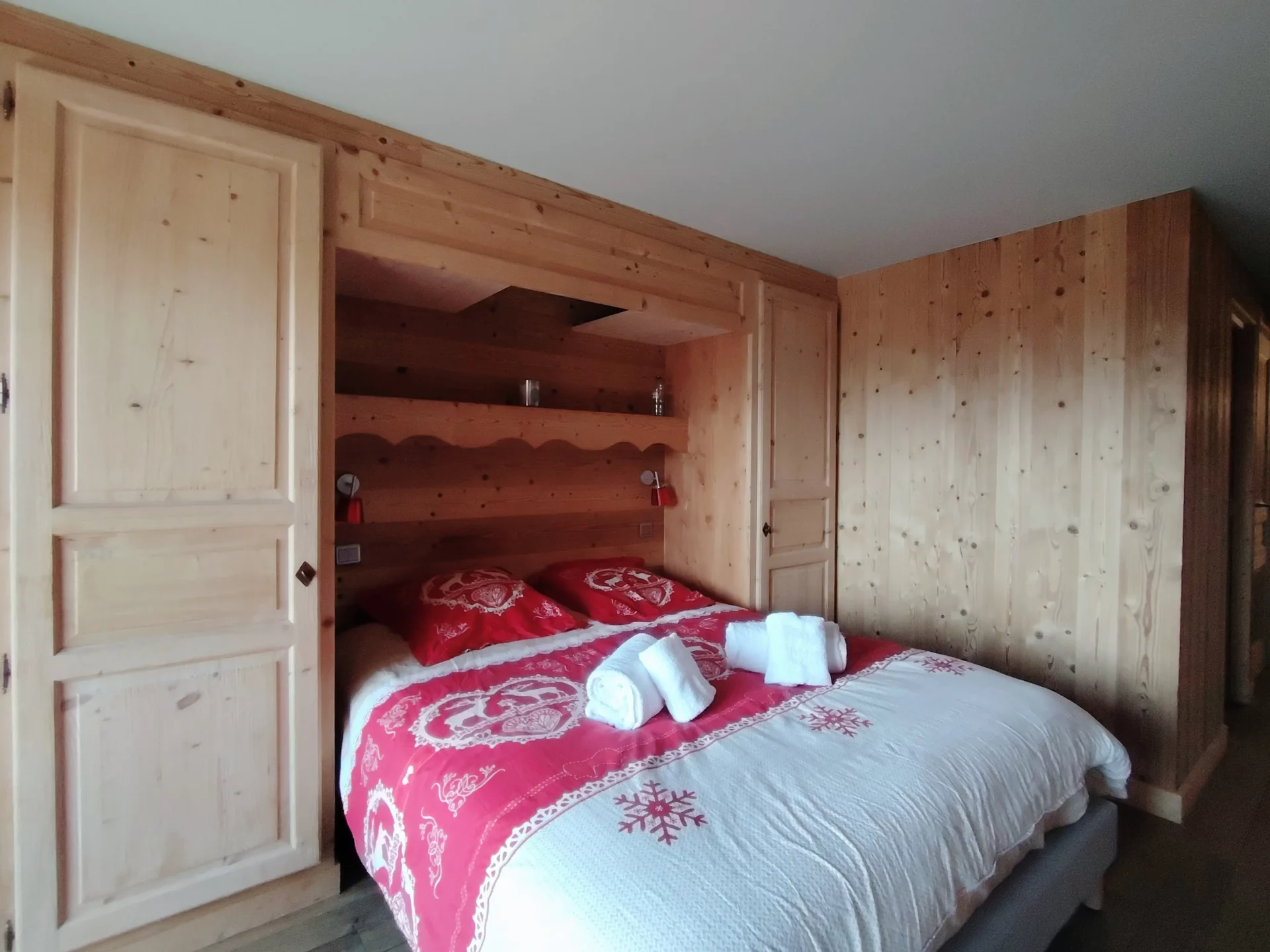 Chambre cosy de l’appartement Les Alpages à l’Alpe d’Huez, grand lit double, rangements intégrés et ambiance chalet en bois