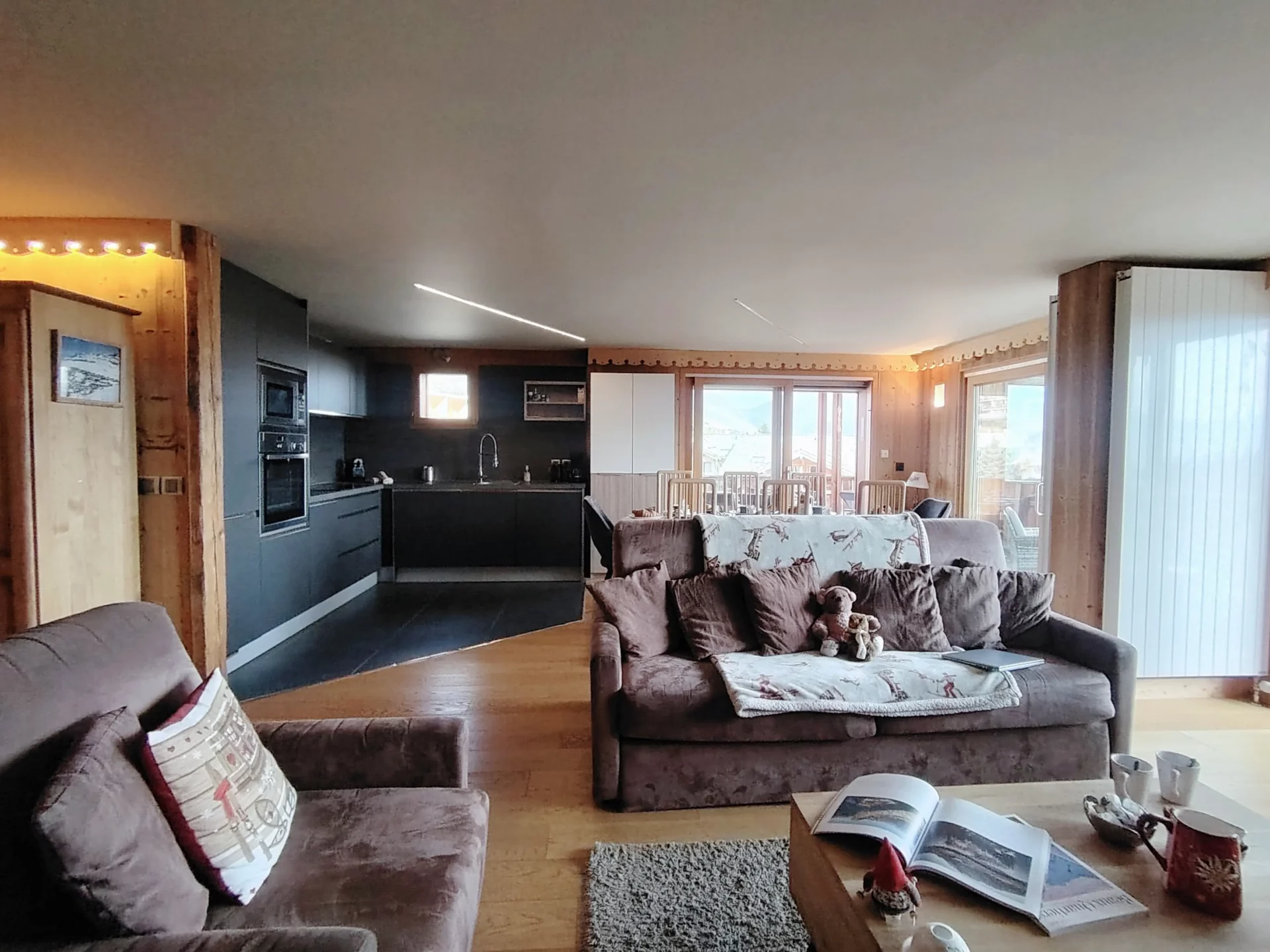 Appartement Les Alpages Alpe d’Huez – séjour spacieux avec cuisine moderne ouverte, coin salon cosy et grande luminosité naturelle.