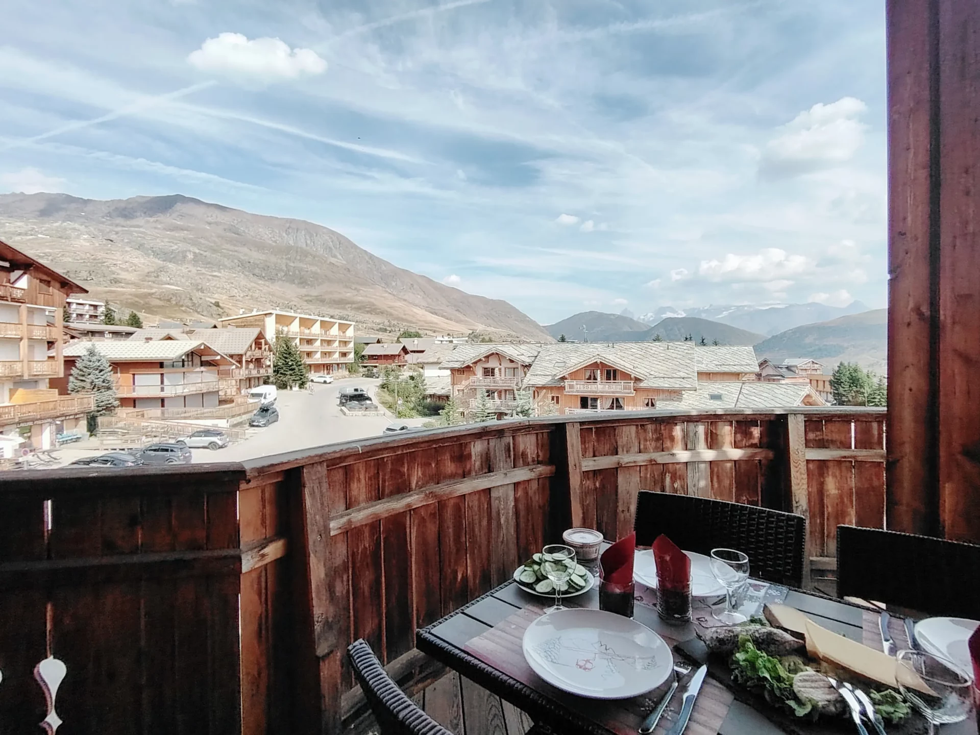 Terrasse de l’appartement Les Alpages à l’Alpe d’Huez, table dressée avec vue panoramique sur les montagnes et chalets alpins