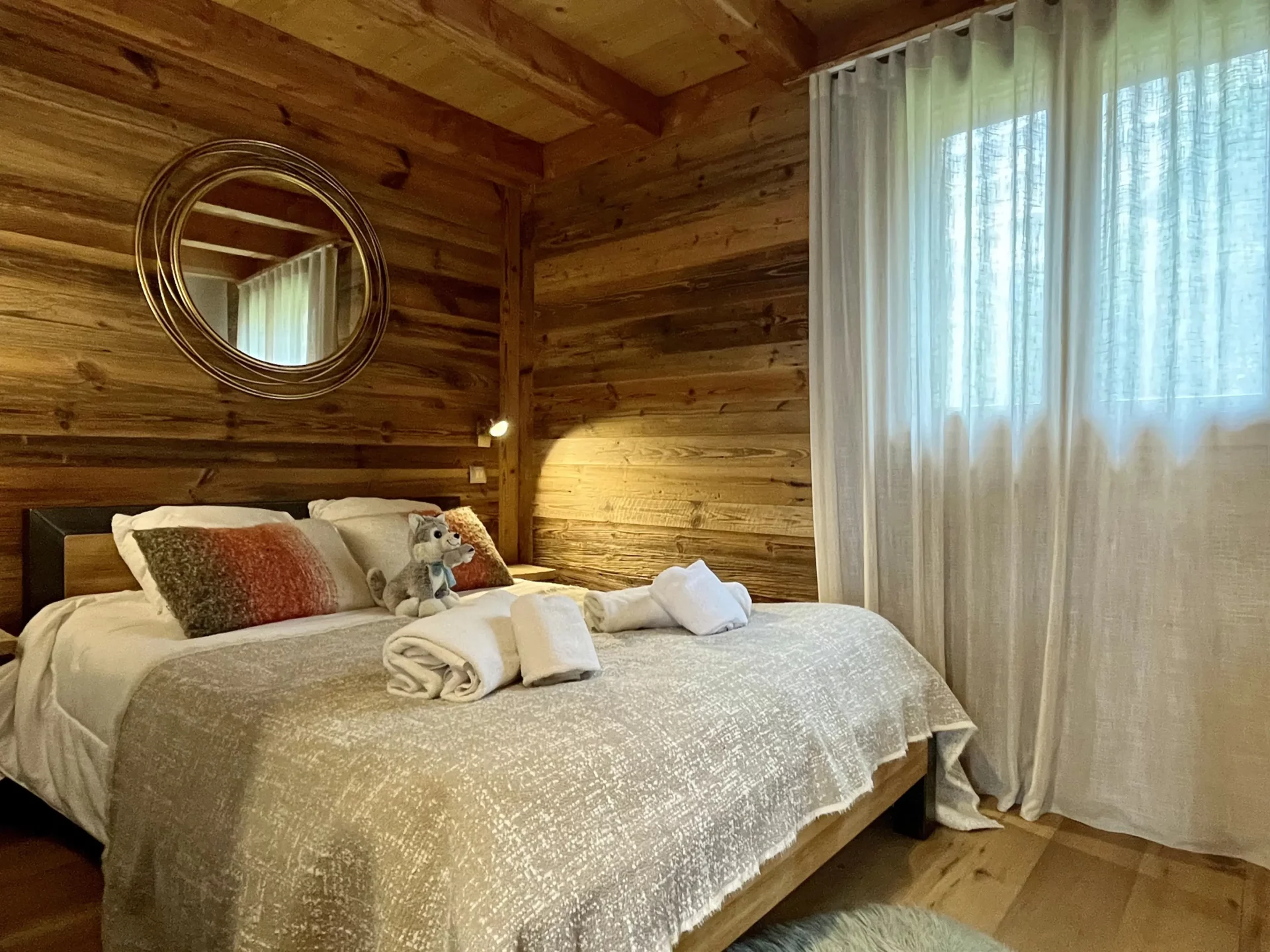 Chambre parentale cosy avec décoration bois et miroir rond – Résidence Ourson Alpe d’Huez