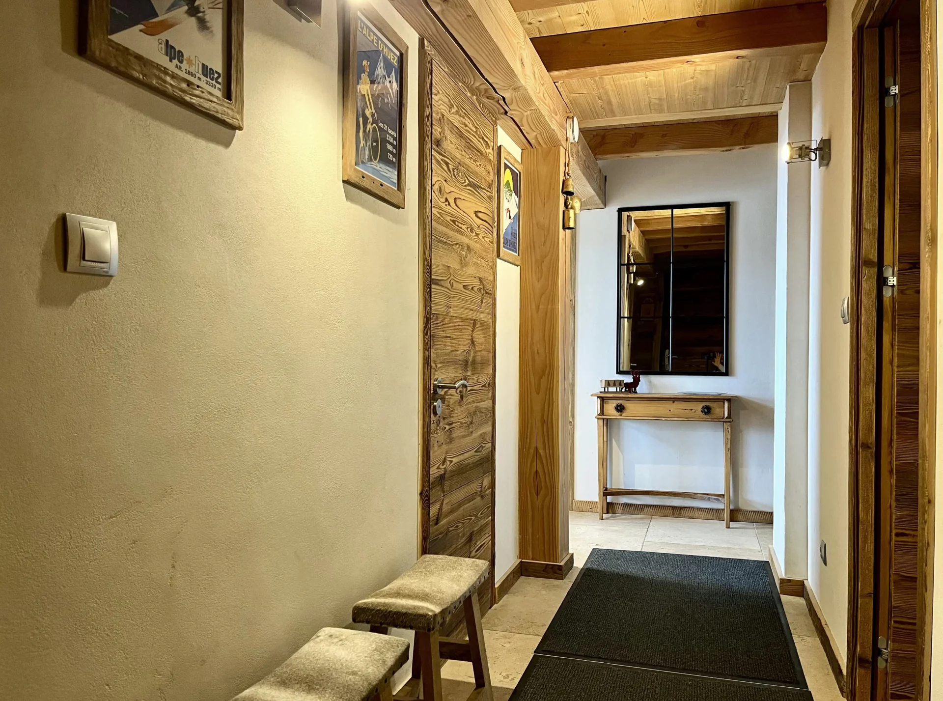 Couloir décoré avec affiches vintage de l’Alpe d’Huez et mobilier en bois.