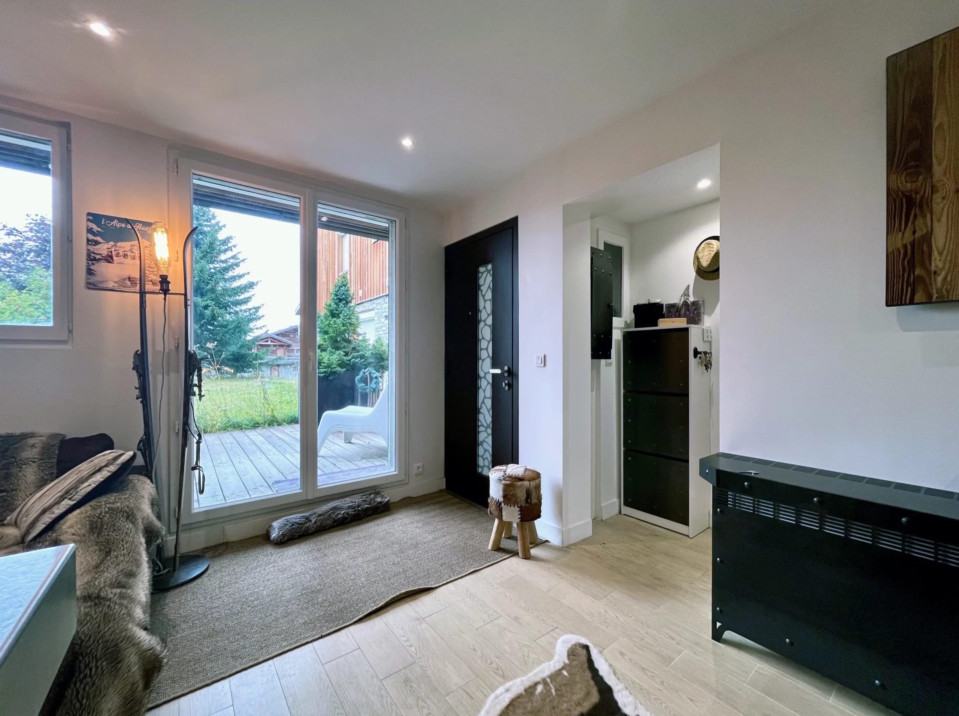 Entrée du Chalet Isba à l’Alpe d’Huez, ouverte sur la terrasse et le salon, avec mobilier de rangement et décoration montagnarde discrète.