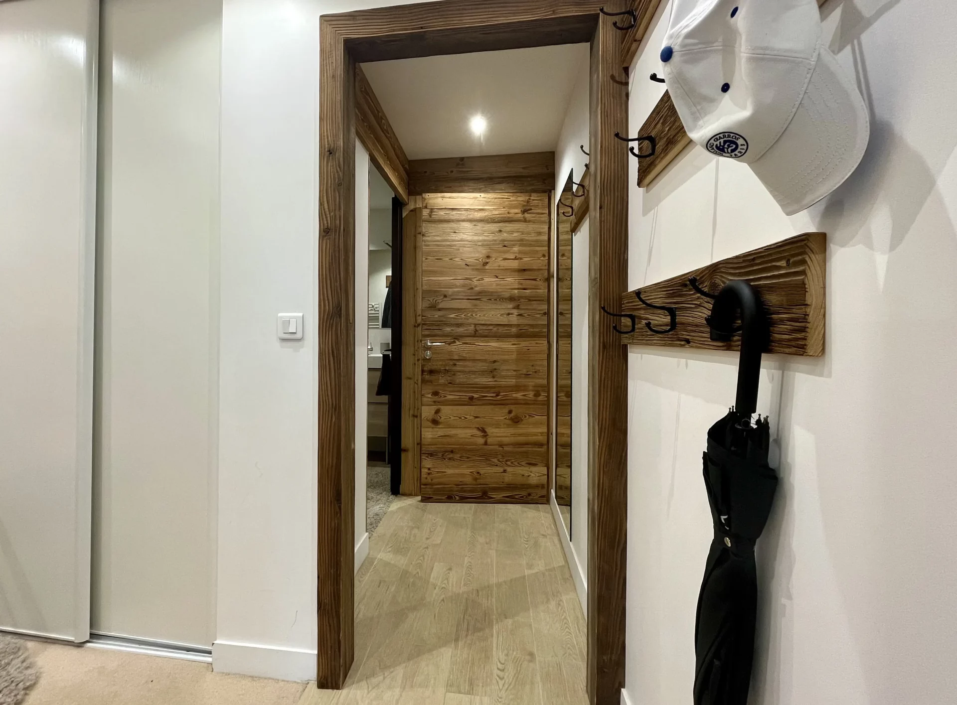 Couloir du Chalet Isba à l’Alpe d’Huez, avec portes en bois massif, patères murales et encadrement en bois naturel typique des chalets alpins.