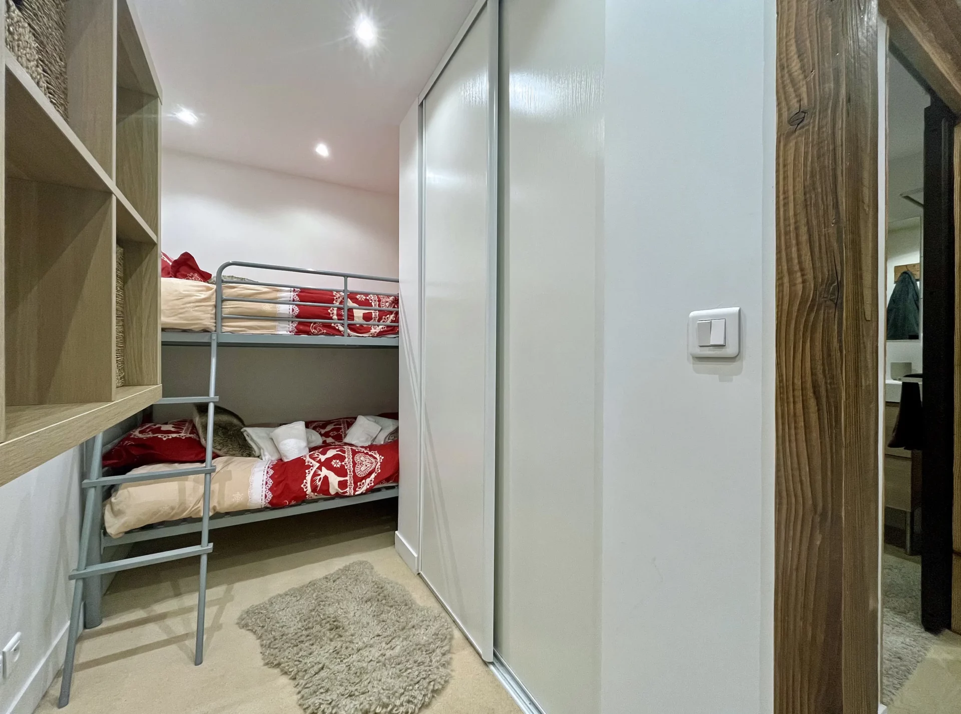 Coin montagne du Chalet Isba, avec lits superposés en métal, parure de lit rouge et blanche à motifs savoyards et rangements intégrés.