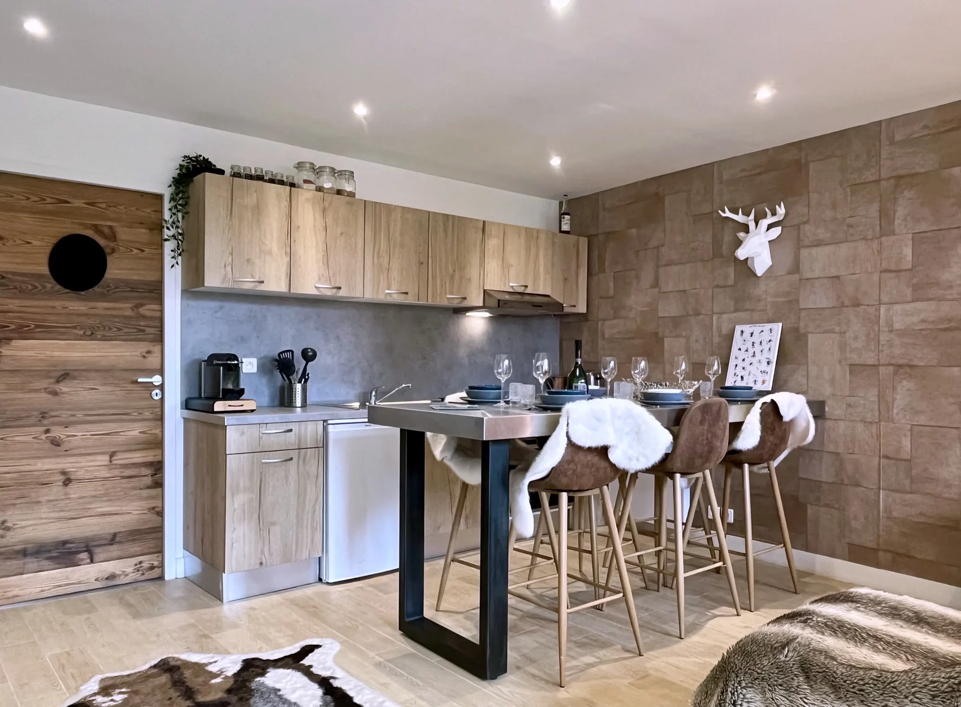 Cuisine moderne du Chalet Isba, composée de rangements en bois, plan de travail en pierre et table haute avec vaisselle dressée pour quatre personnes.