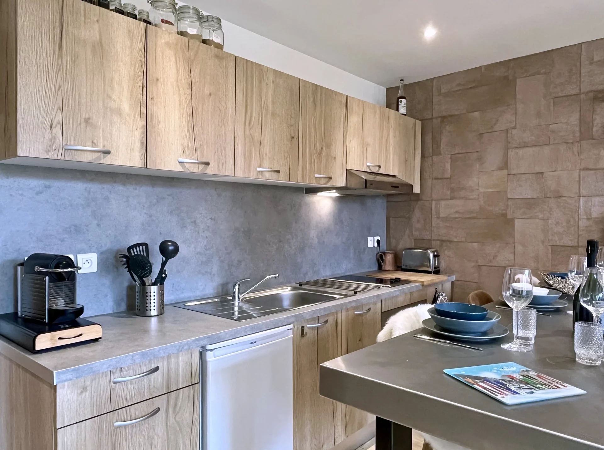Détail de la cuisine équipée du Chalet Isba à l’Alpe d’Huez, avec plaque de cuisson, évier inox, Nespresso et ustensiles de cuisine modernes.