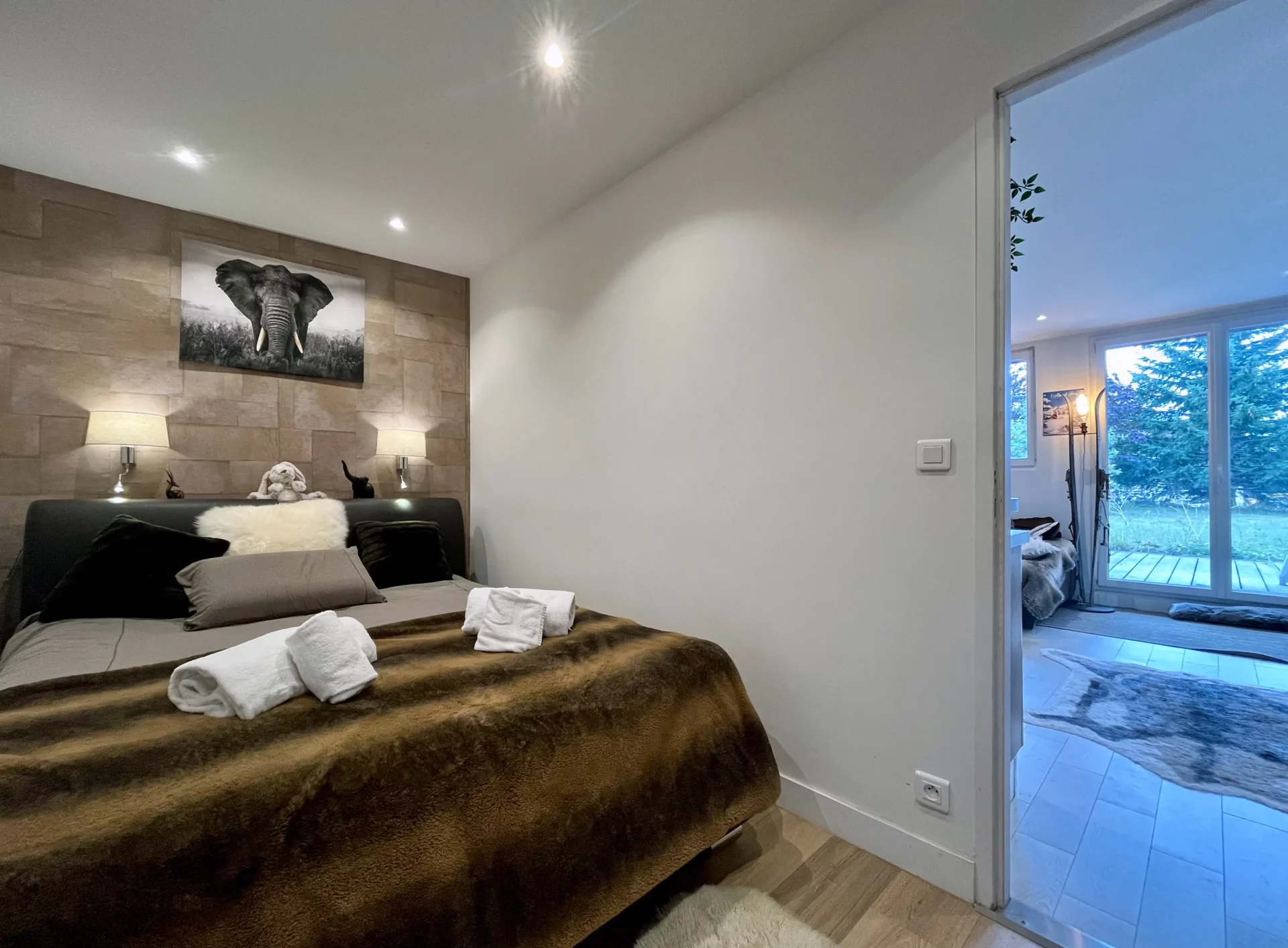 Chambre double du Chalet Isba à l’Alpe d’Huez, lit 160 cm recouvert d’une couverture en fausse fourrure, ambiance douce et vue sur le salon.