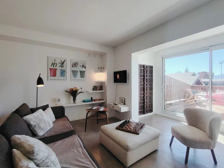 Séjour lumineux avec canapé et fauteuil donnant accès à la terrasse – appartement Alpe d’Huez