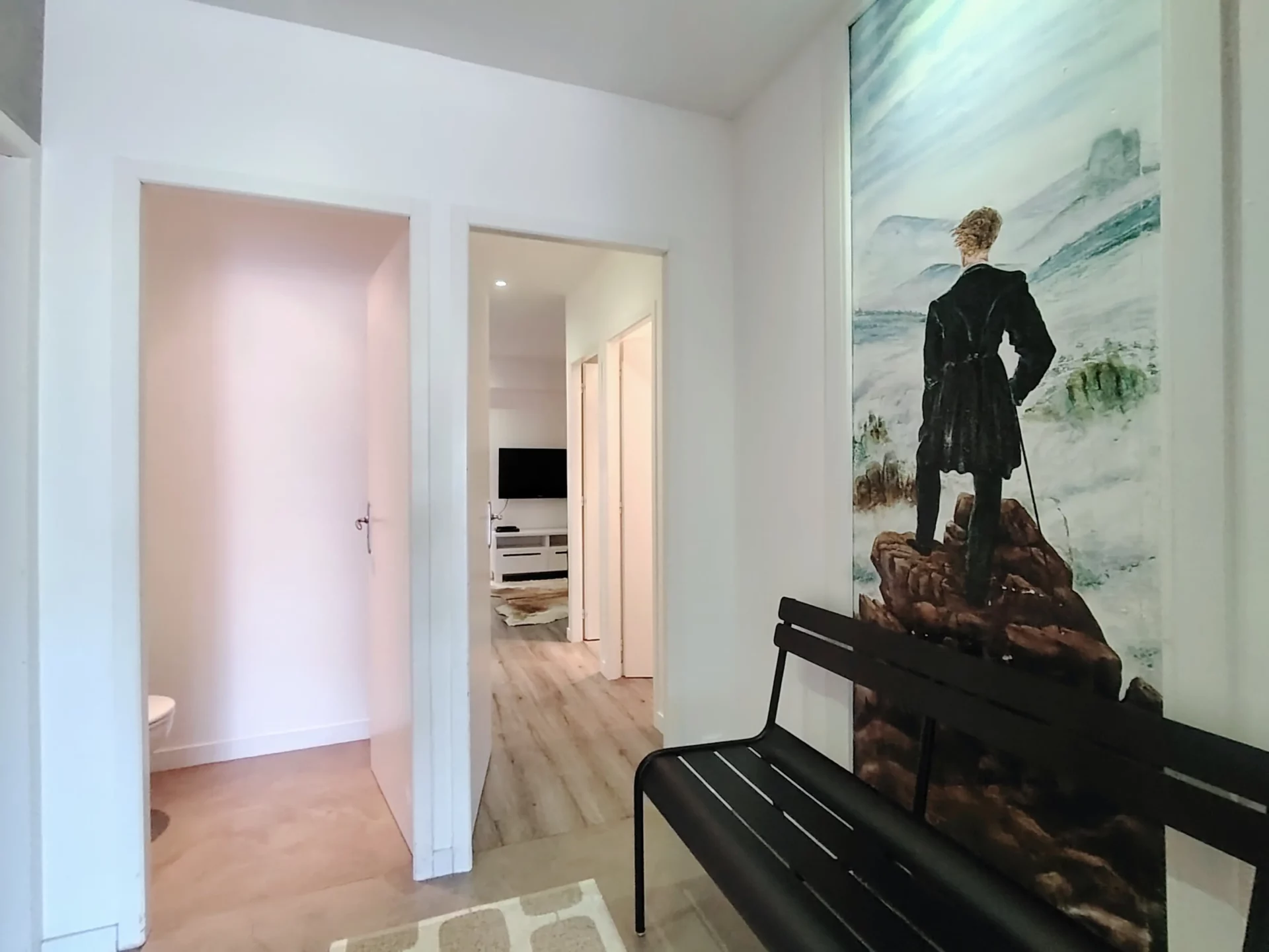Entrée lumineuse de l’appartement avec banc design et fresque murale représentant un paysage alpin.