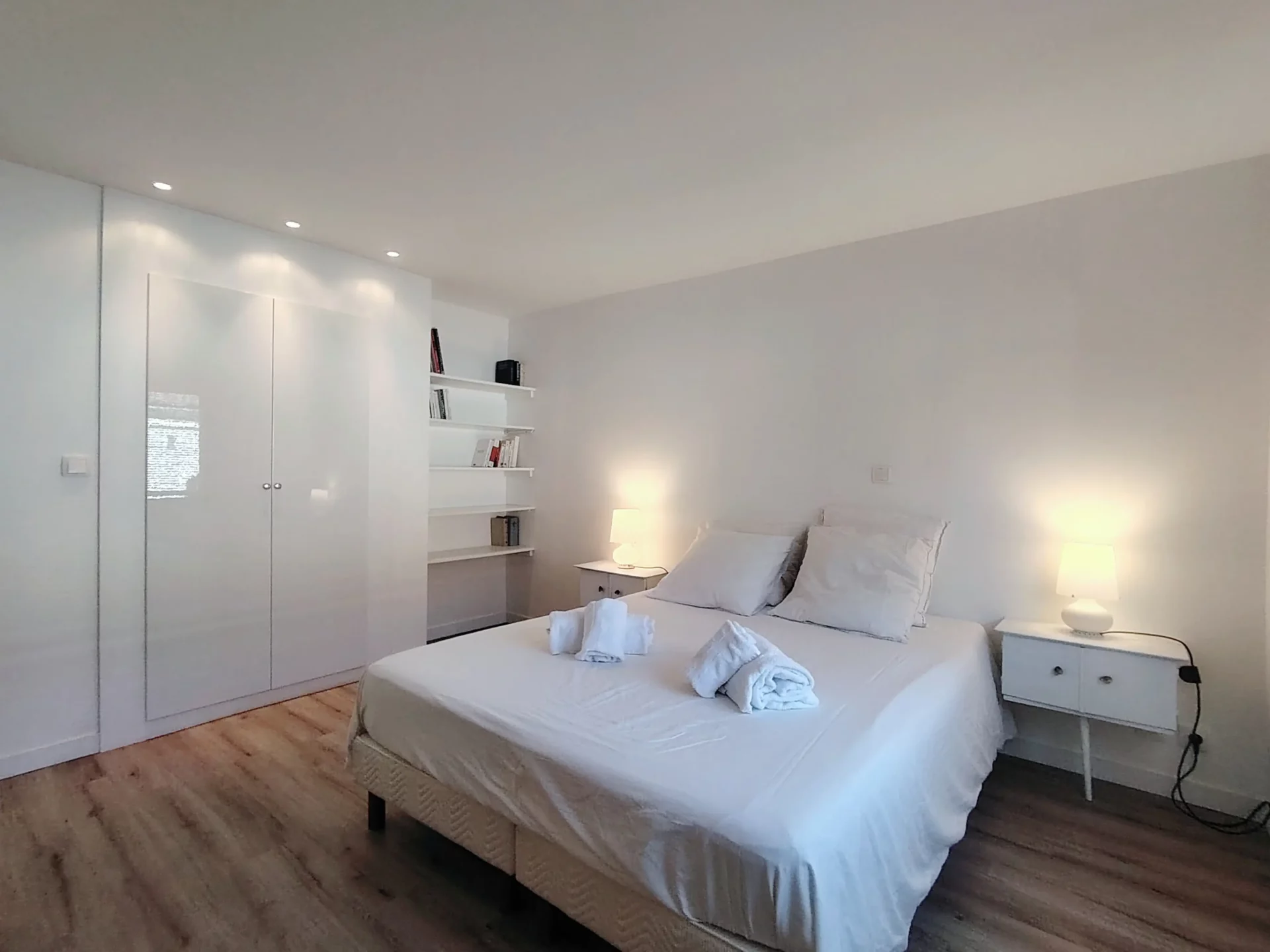 Chambre double spacieuse avec lit queen size, armoires blanches intégrées et étagères murales.