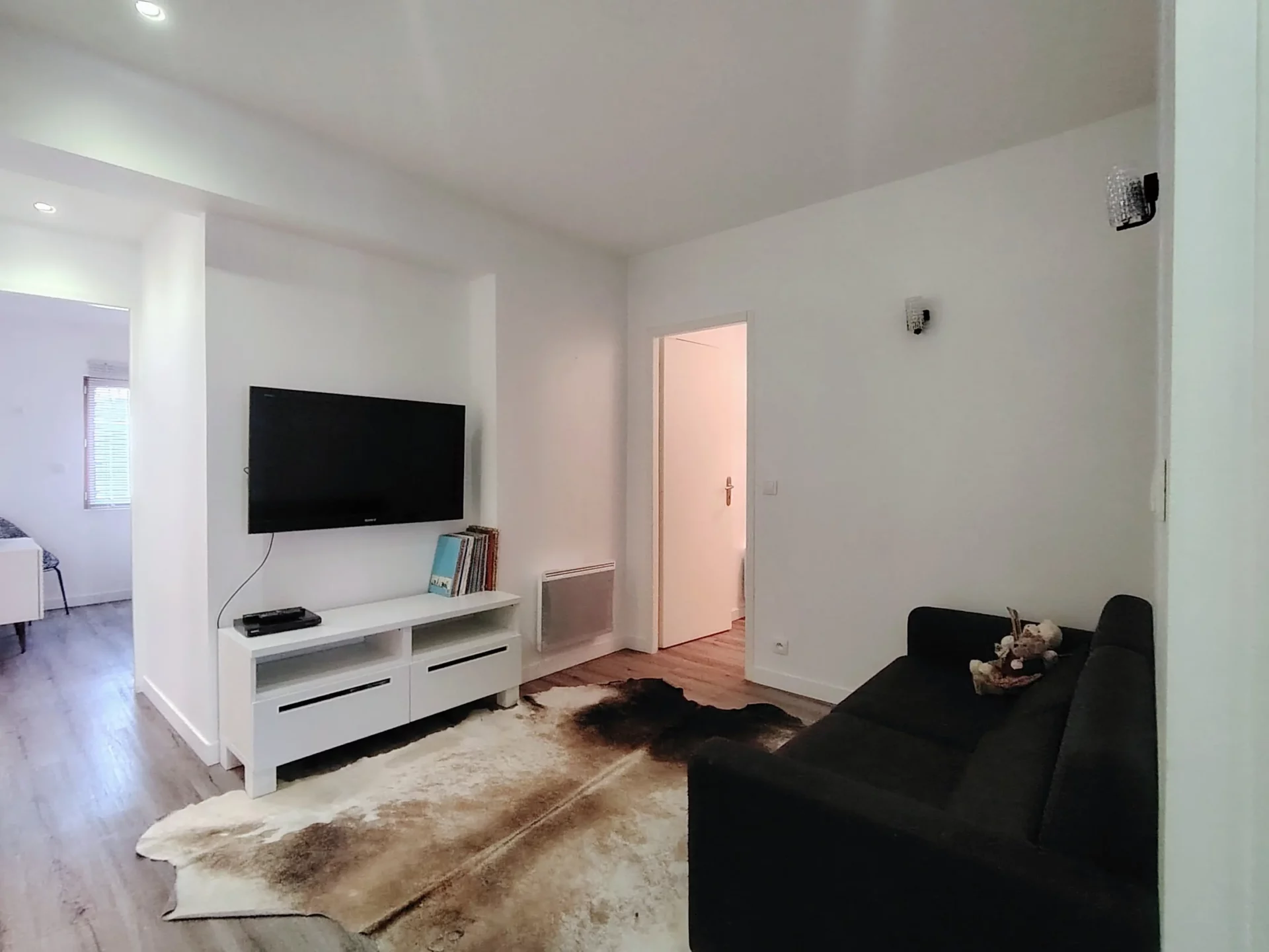 Salon cosy avec canapé noir, TV écran plat et coin lecture – Appartement Résidence Ménandière H1 Alpe d’Huez