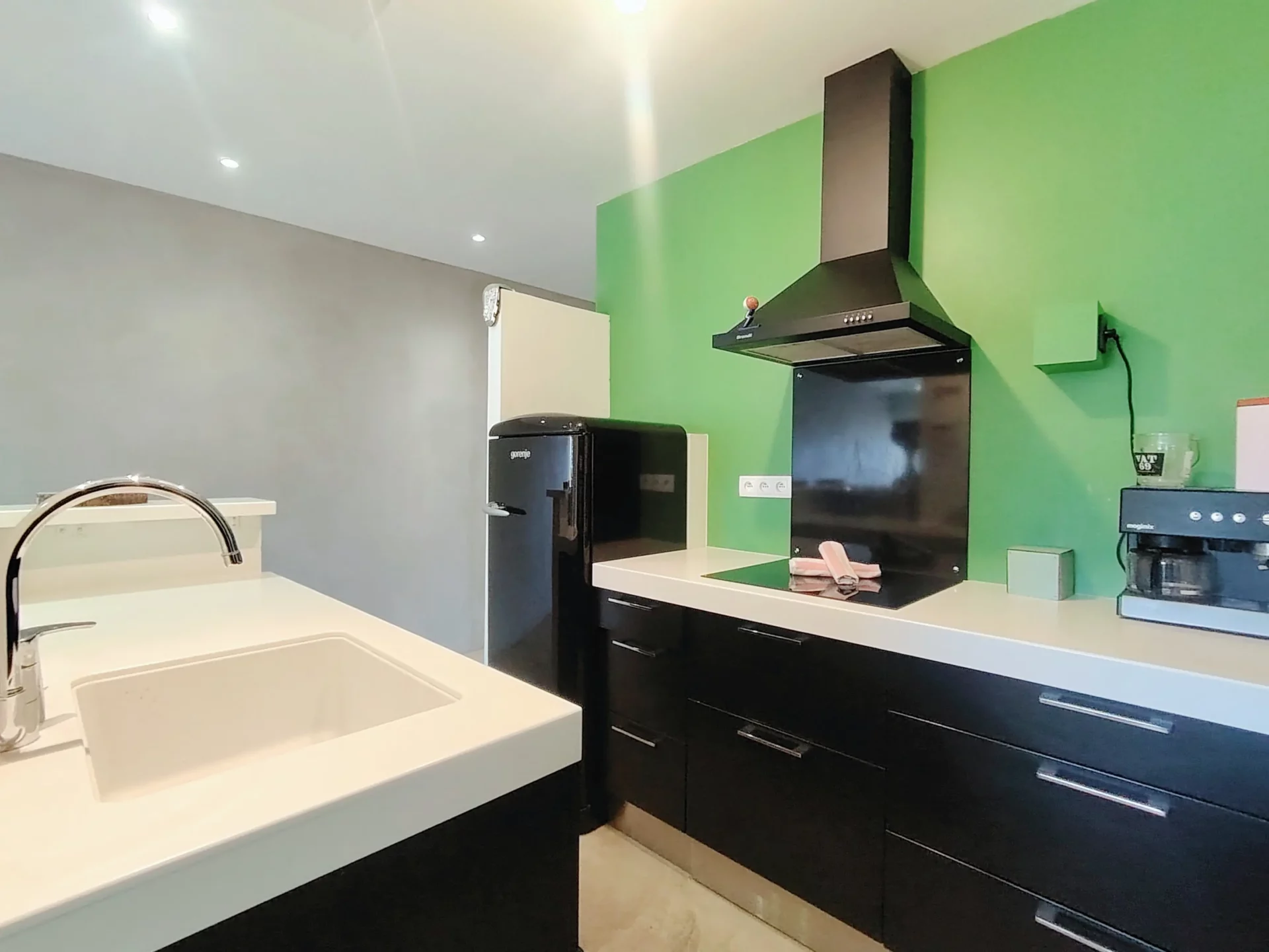Cuisine moderne avec plan de travail blanc, hotte noire et mur vert – appartement Alpe d’Huez