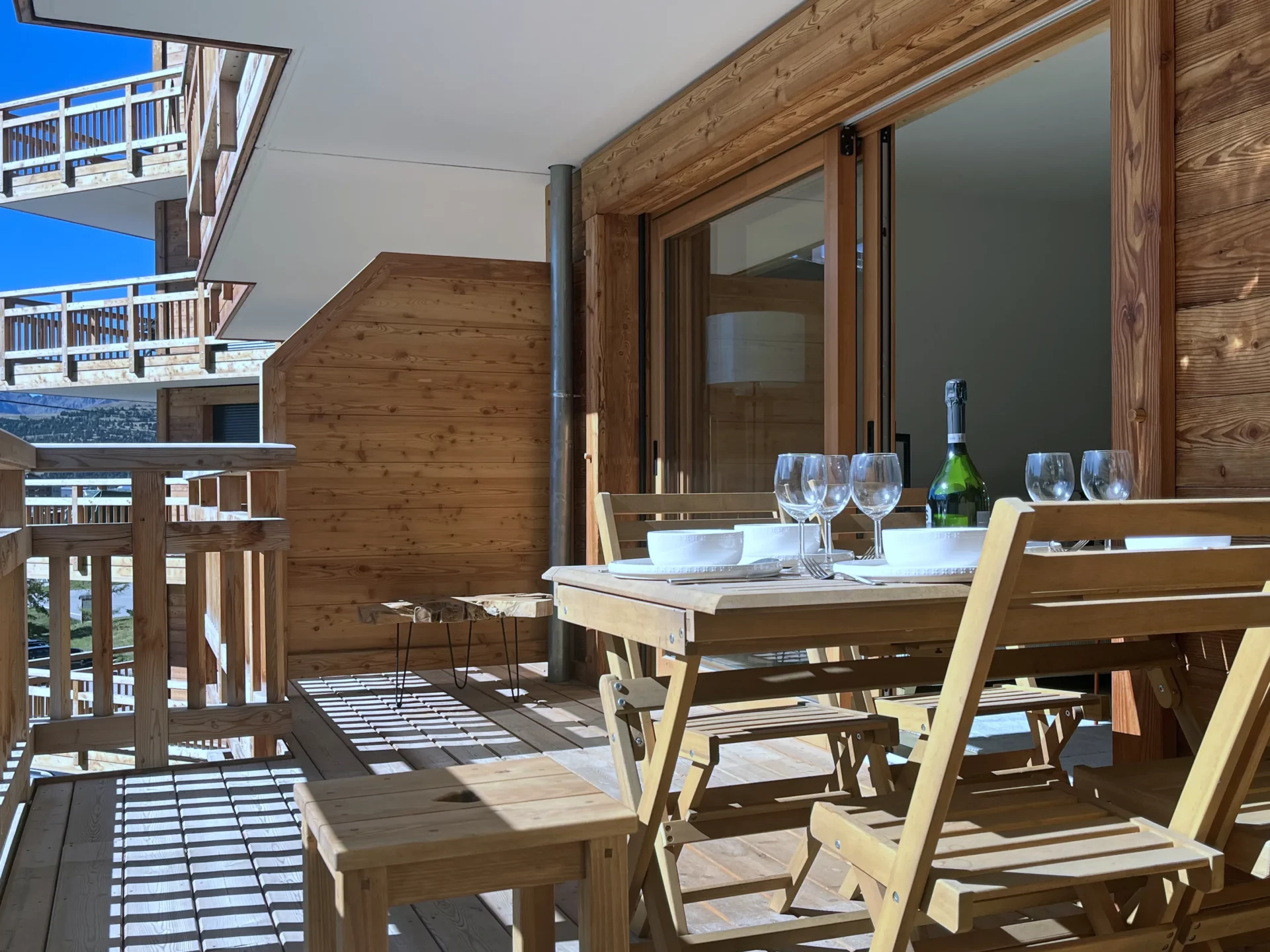 Terrasse ensoleillée avec mobilier en bois et vue sur les chalets voisins à l’Alpe d’Huez, résidence Cachemire.