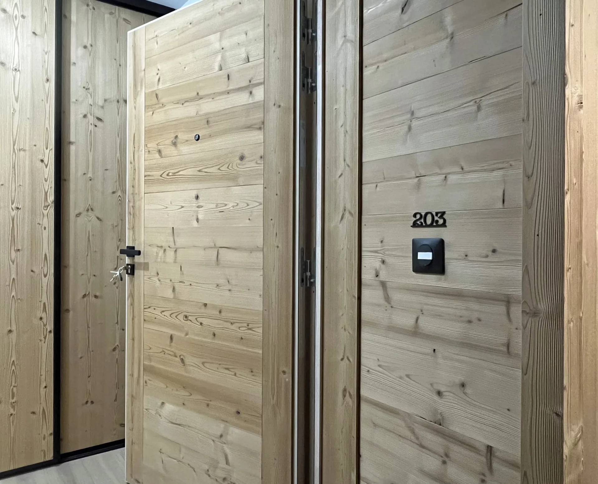 Porte d’entrée en bois clair numérotée 203, dans le couloir moderne de la résidence Cachemire à l’Alpe d’Huez.