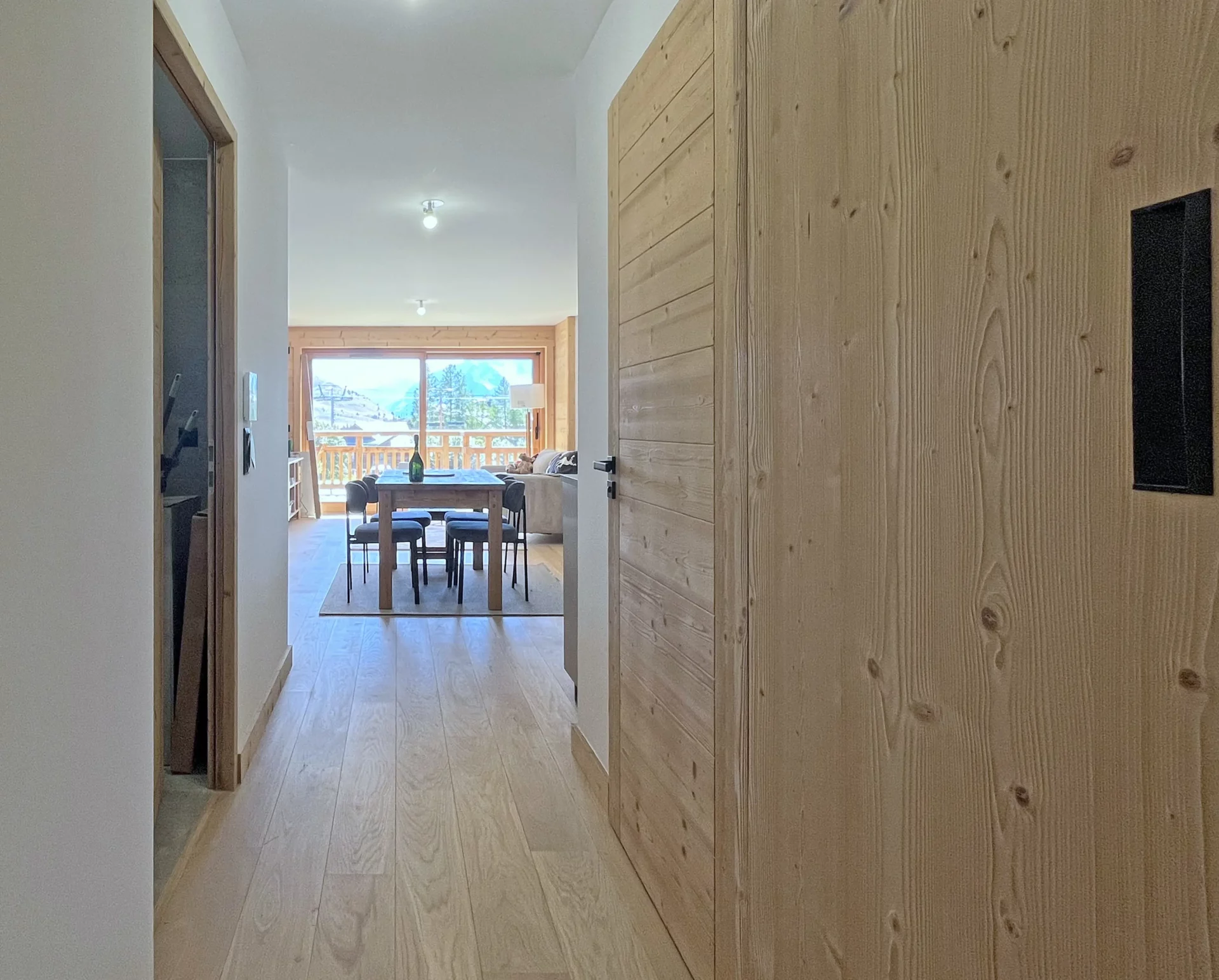 Couloir intérieur lumineux avec sol en bois clair et porte menant à la pièce de vie ouverte sur la terrasse.