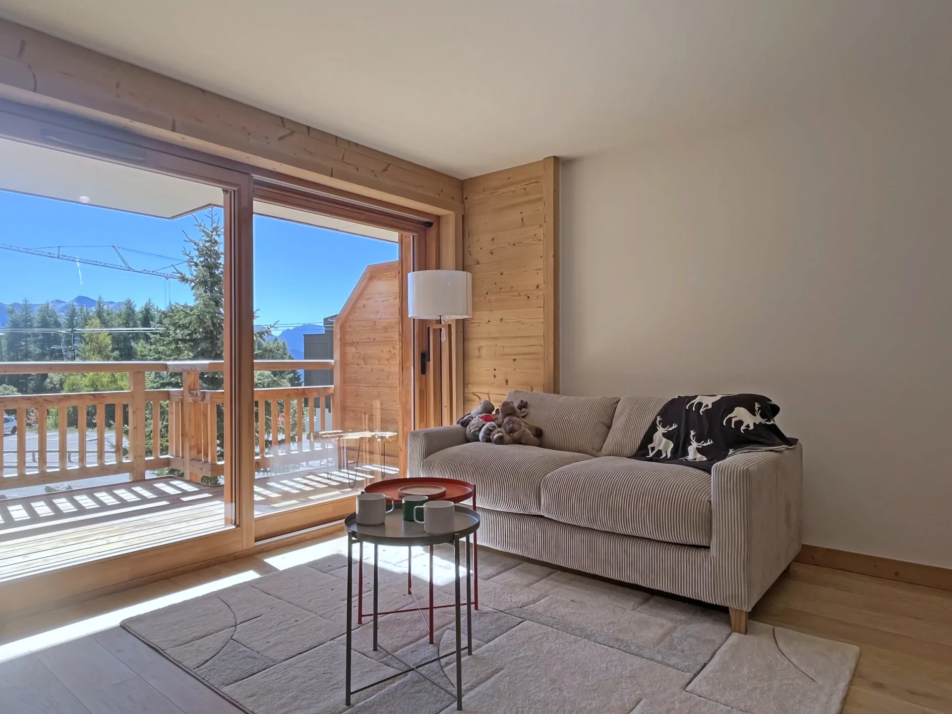 Canapé confortable près d’une grande fenêtre ouvrant sur une terrasse en bois avec une agréable vue montagne.