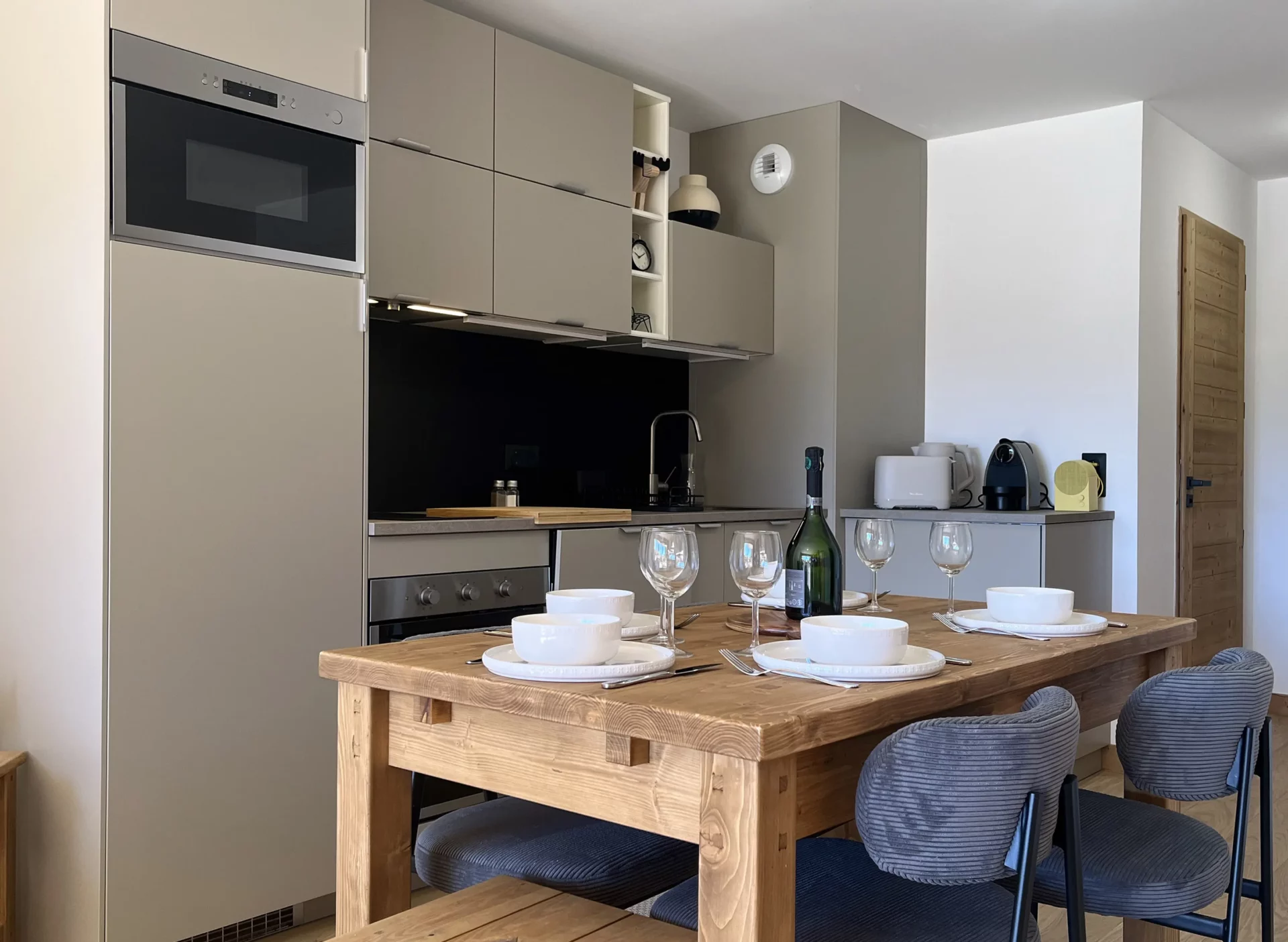 Cuisine contemporaine entièrement équipée avec coin repas en bois et chaises modernes dans un appartement de montagne.