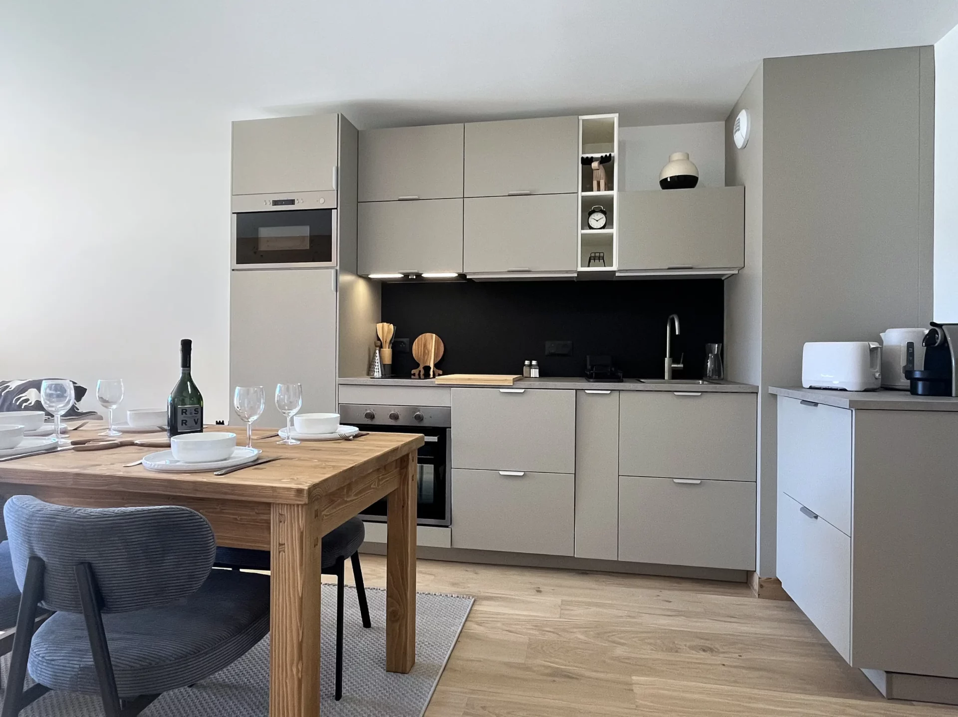 Vue sur la cuisine intégrée et table à manger dressée pour quatre personnes dans un décor bois et tons neutres.